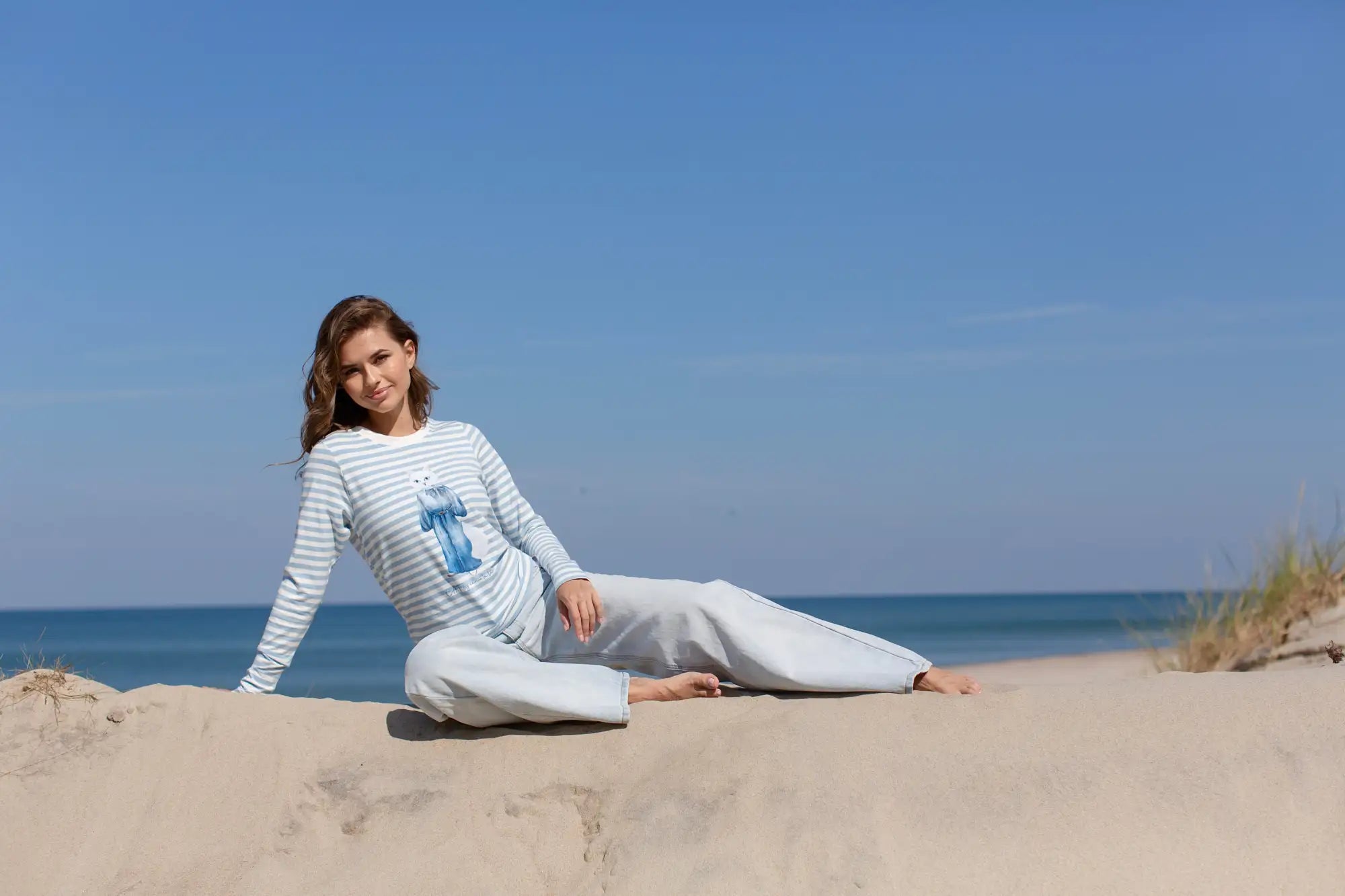 A woman wearing a long-sleeved, light blue and white striped top with a small embroidered graphic on the chest.